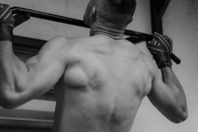 Back view of a shirtless man doing pull-ups, showcasing strength and fitness.