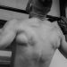 Back view of a shirtless man doing pull-ups, showcasing strength and fitness.